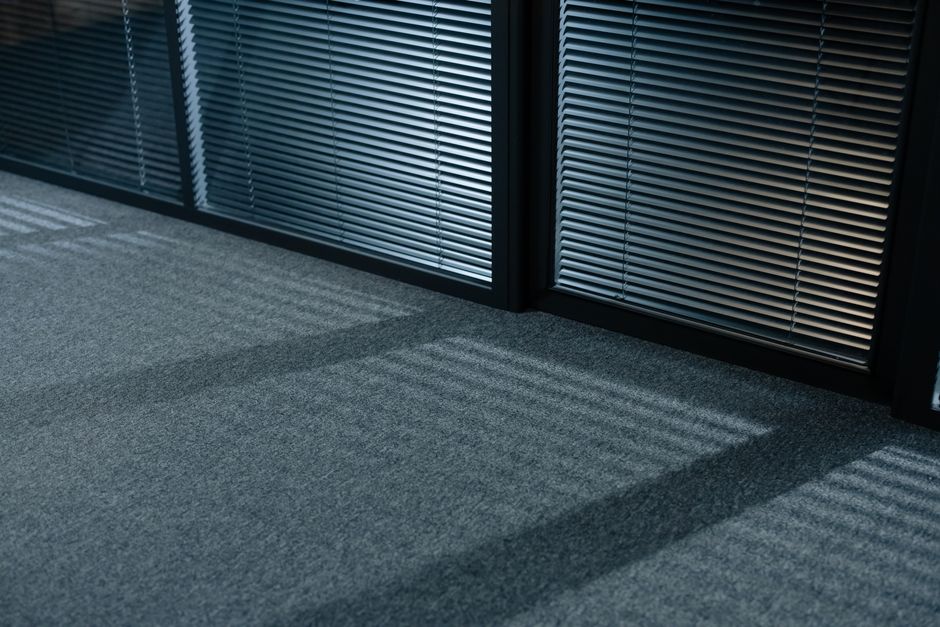 A professional cleaning technician from Redbridge Carpet Cleaners is performing surface cleaning on a beige textured carpet in a modern living room. The technician is wearing white protective coverall